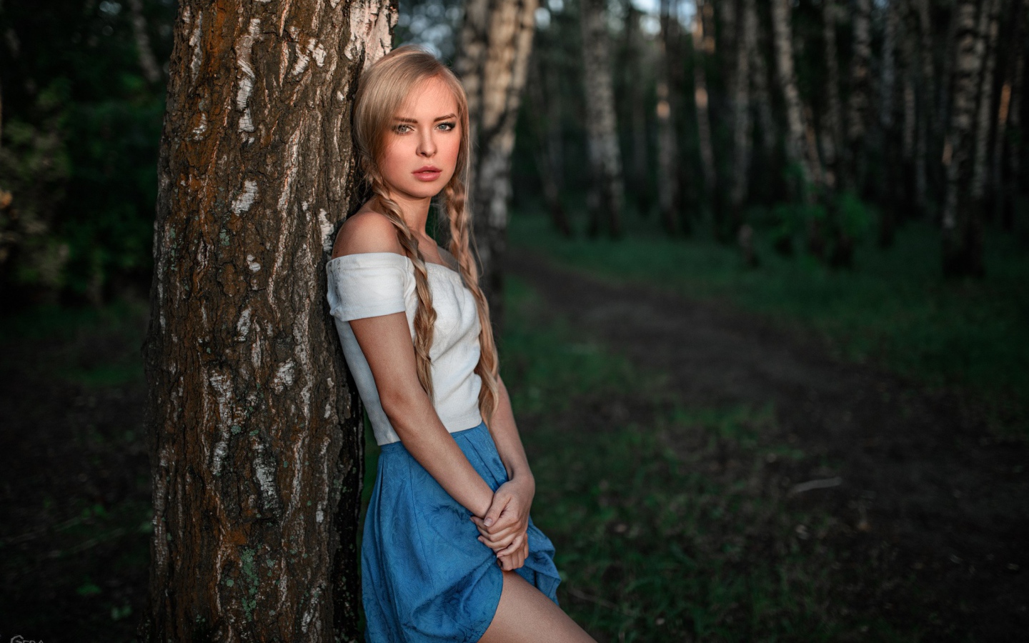 Девушка с русыми косами прислонилась к дереву