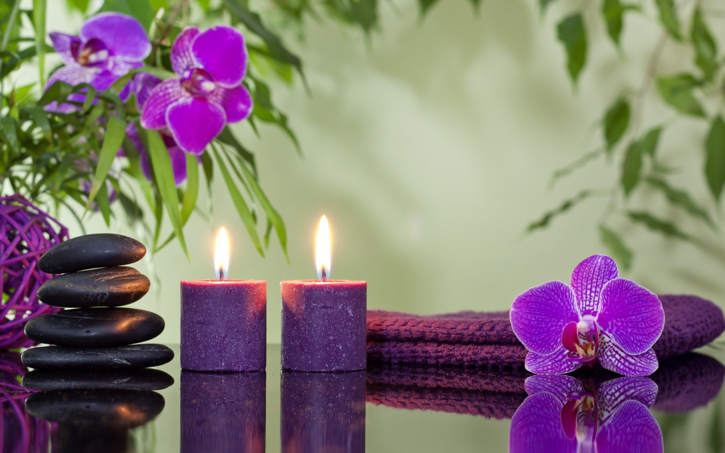 Две горящие свечи с камнями и цветами орхидеи отражаются в зеркальной поверхности стола