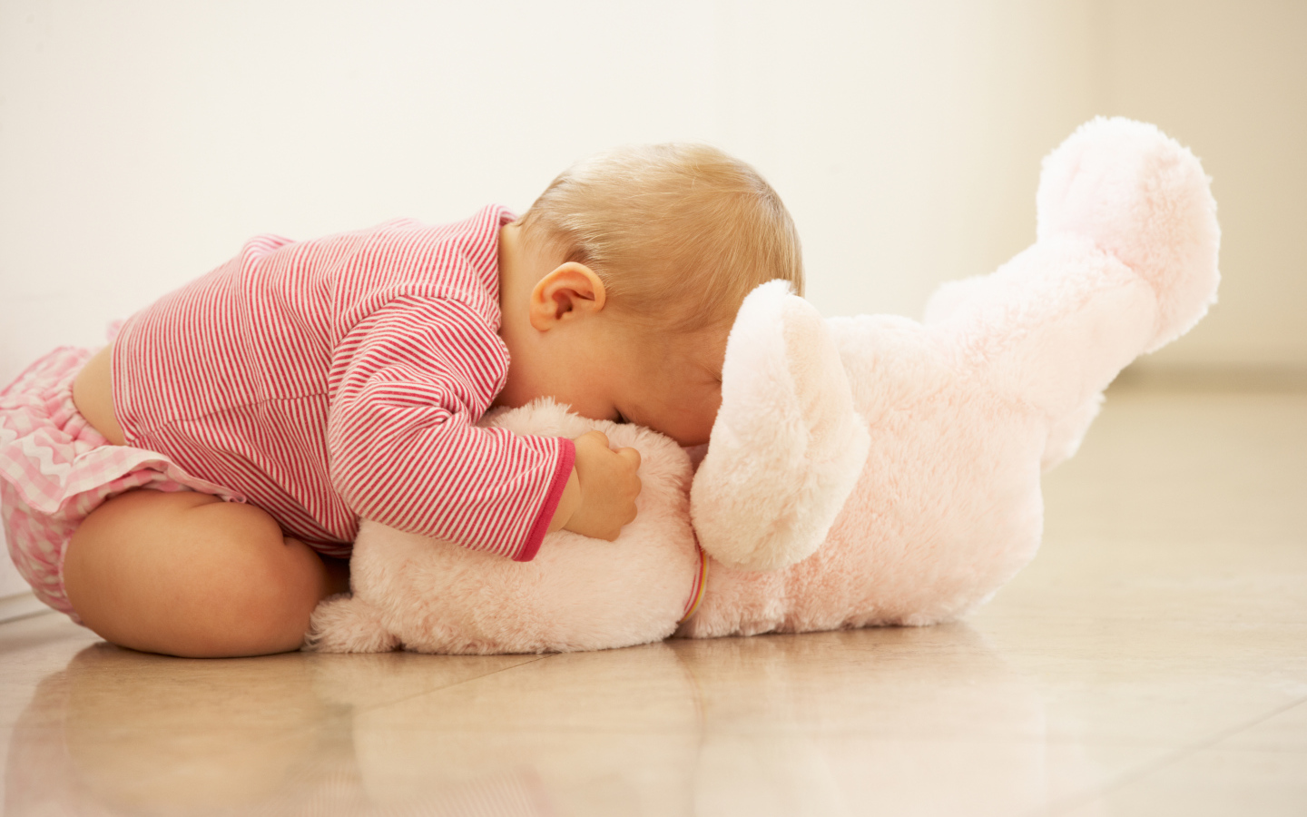 Маленький ребенок играет с розовым игрушечным медведем