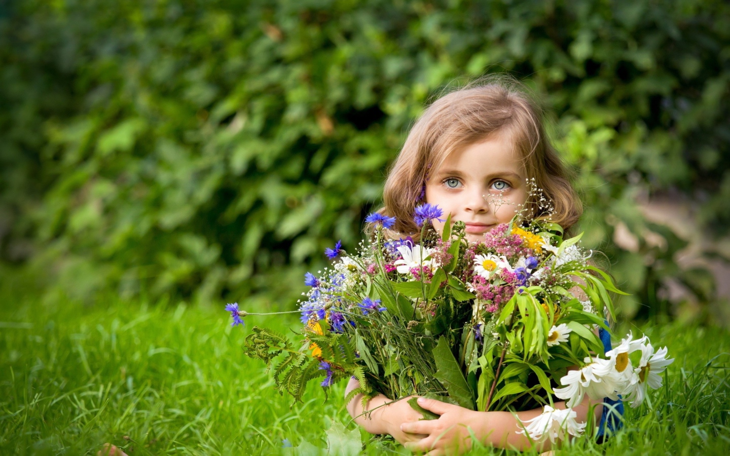 Красивая девочка с букетом цветов лежит на зеленой траве