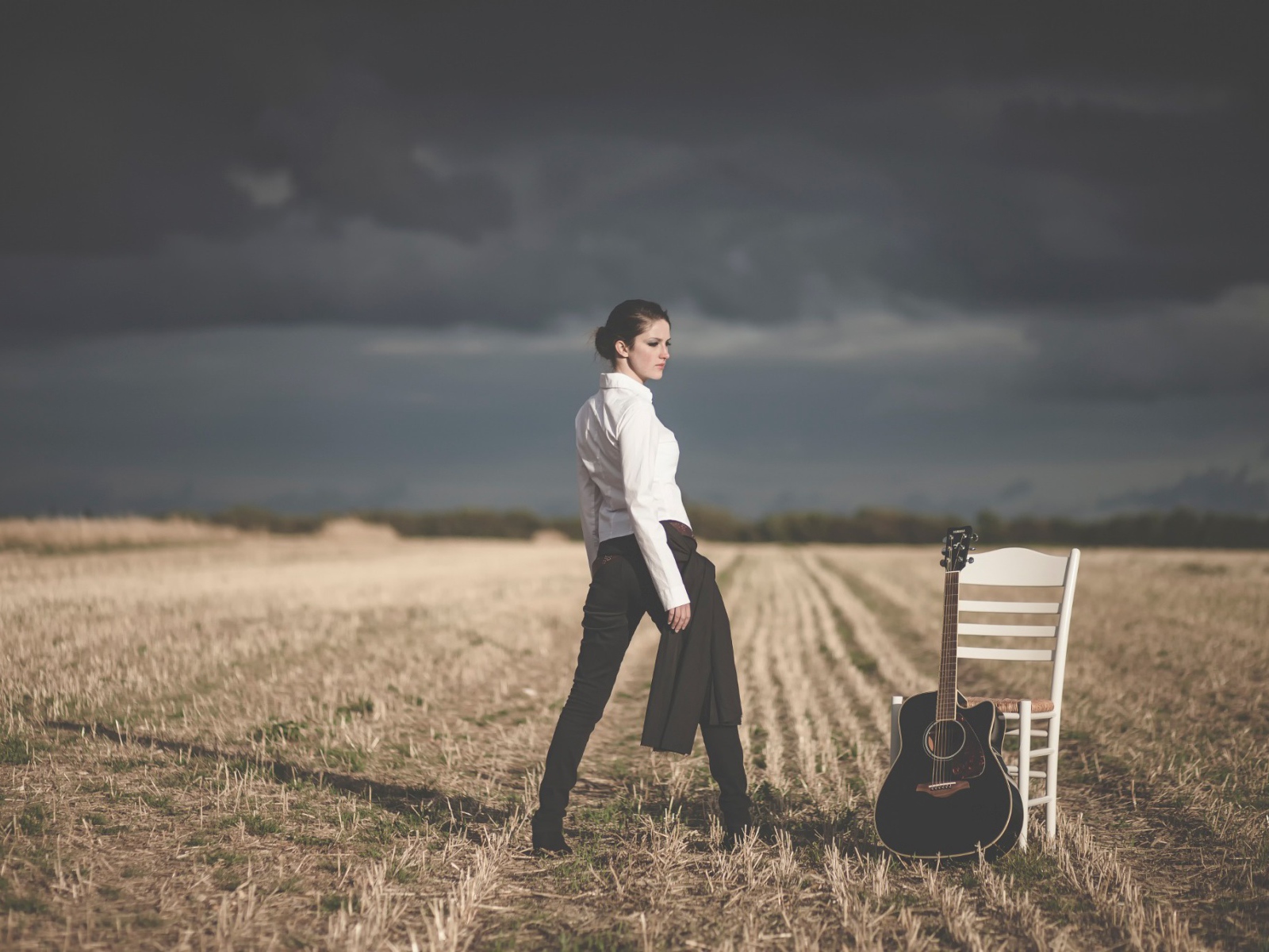 A girl in a field near his chair with a guitar
