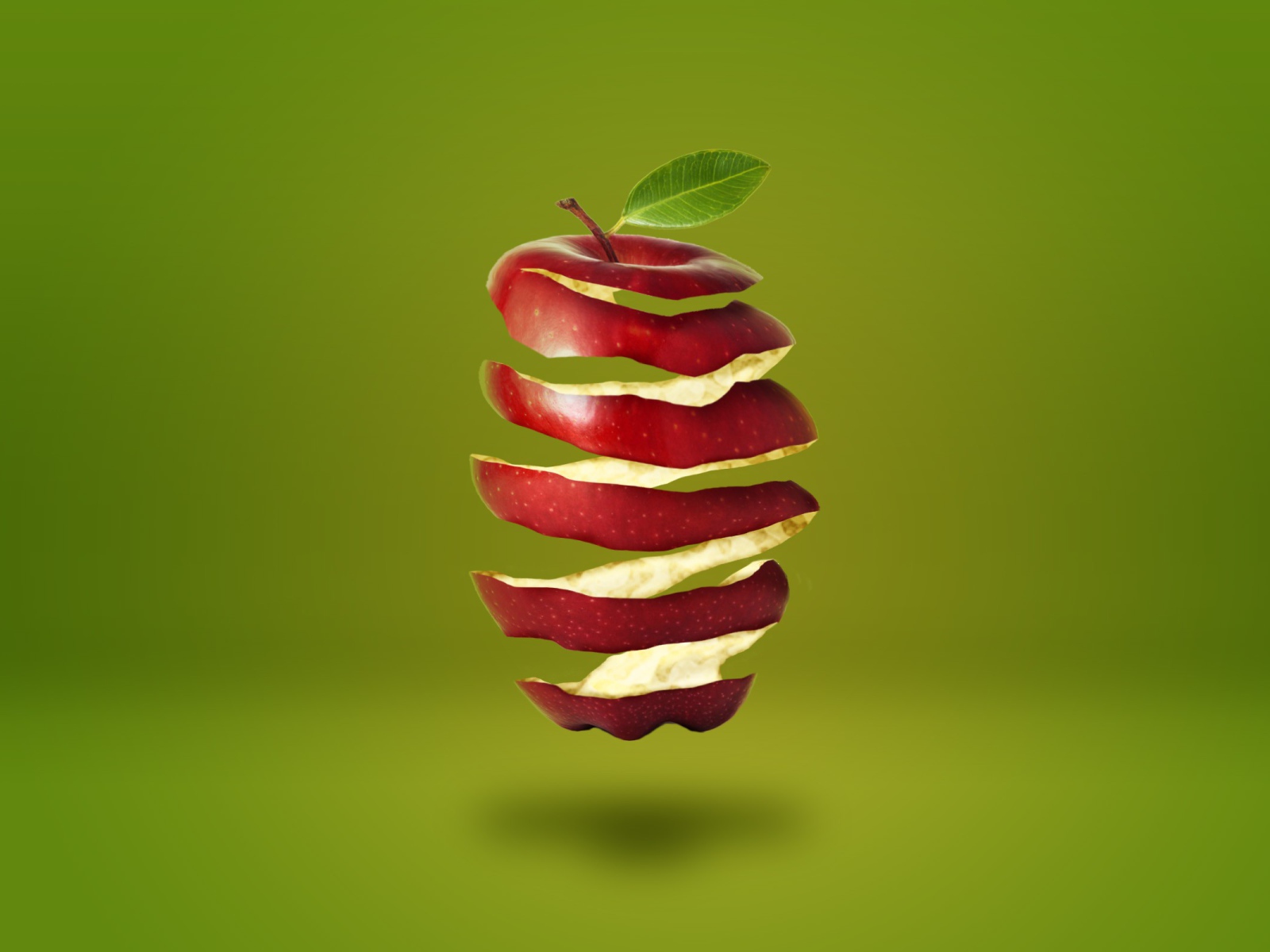 Нарезанное спиралью красное яблоко на зеленом фоне 