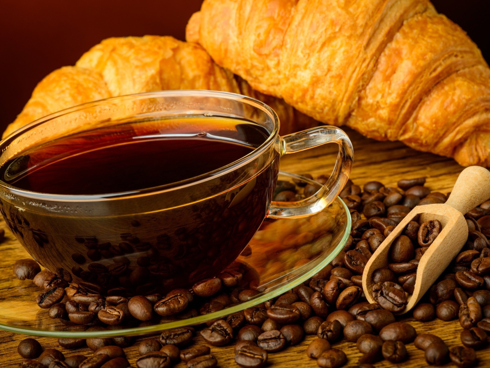 Glass cup of coffee with grains and fresh croissants on the table