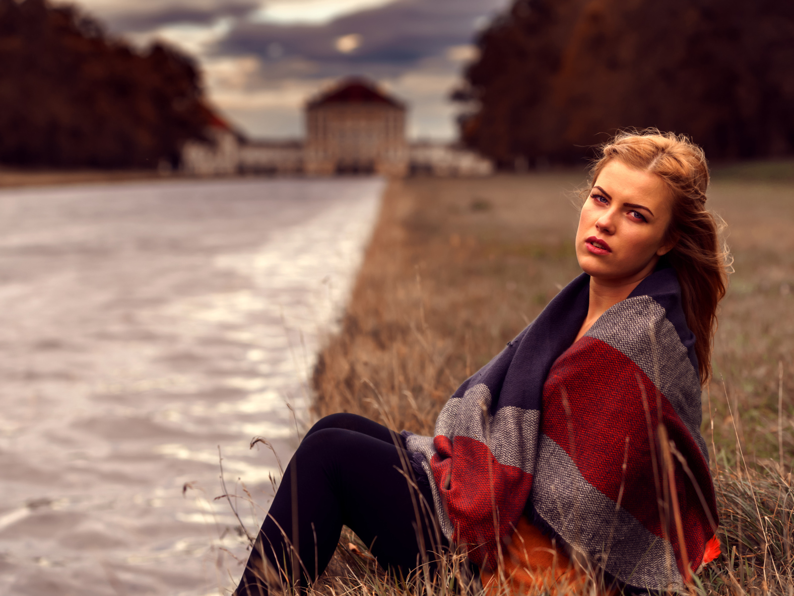 Девушка в пледе сидит на берегу реки