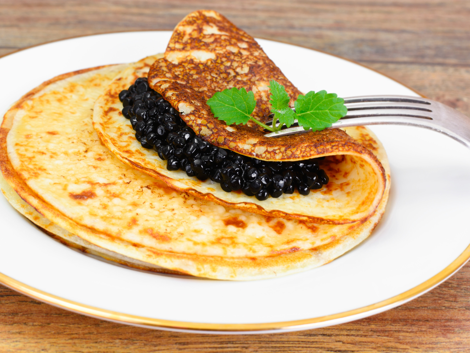 Pancakes with black caviar on a plate with a fork