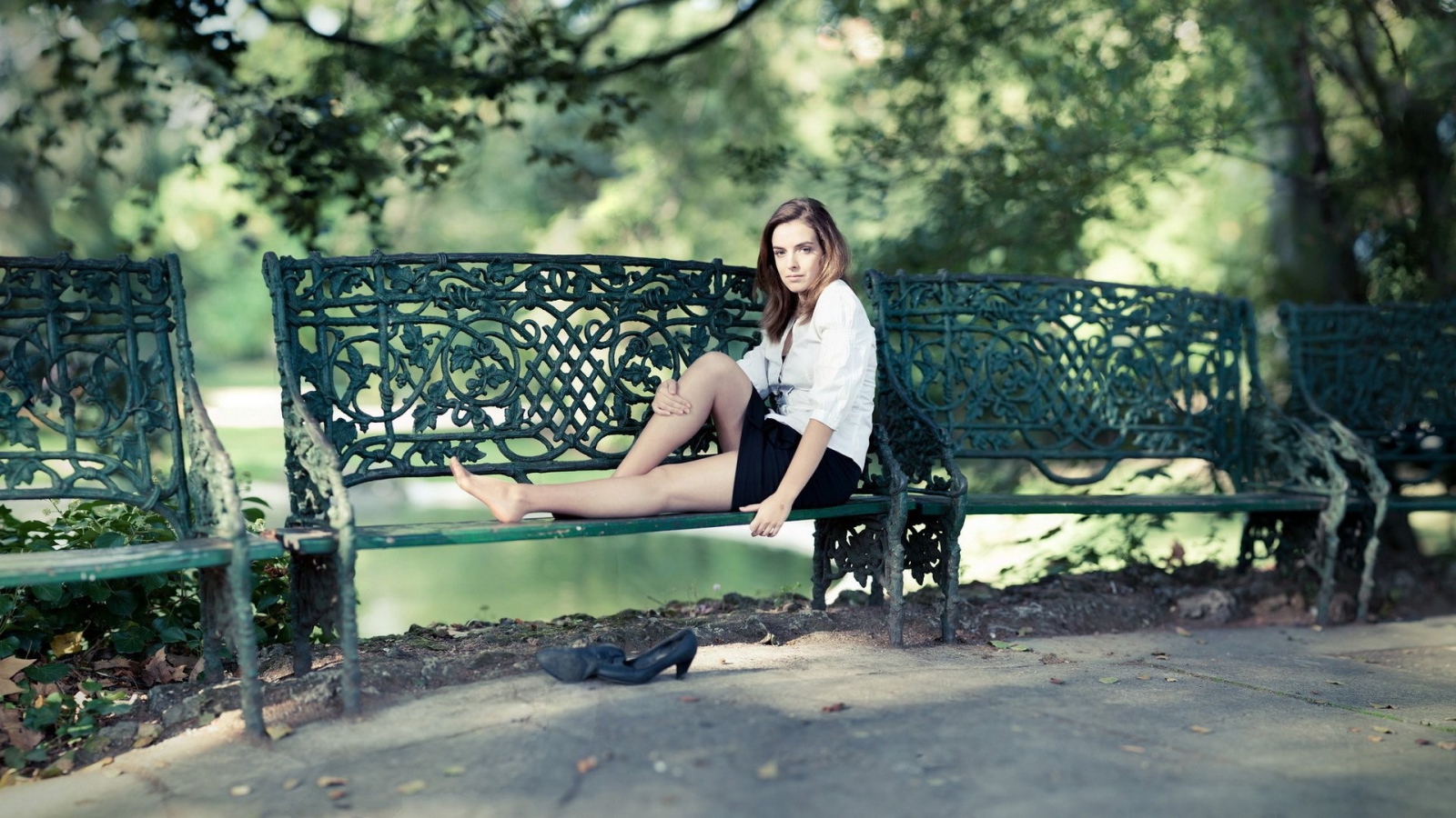 Девушка сидит на кованной парковой скамье