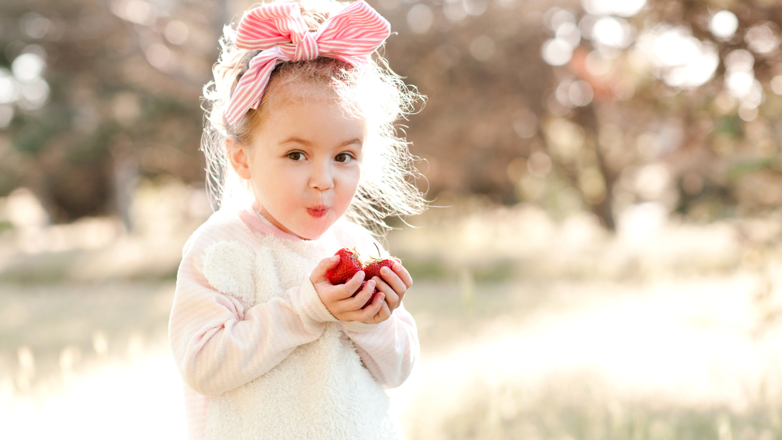 Маленькая девочка с бантом на голове ест клубнику