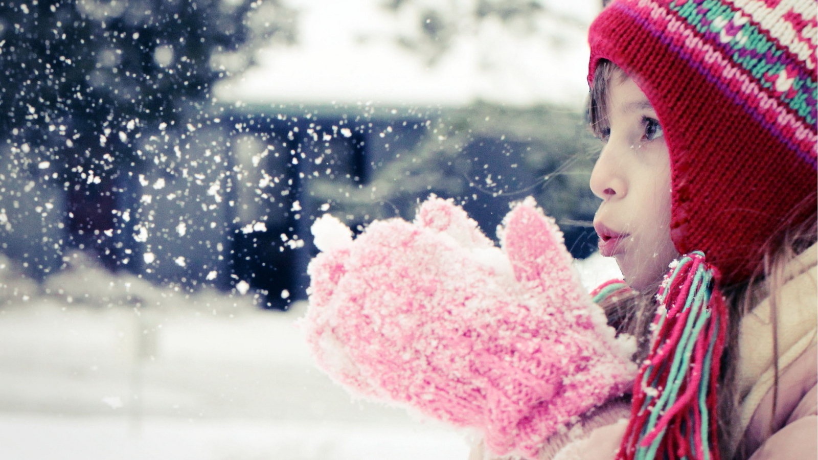 Девочка сдувает белый снег с варежек 