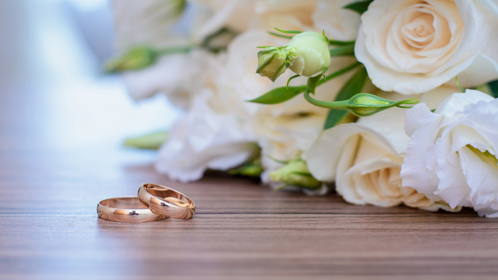 Букет белых роз на столе с золотыми обручальными кольцами
