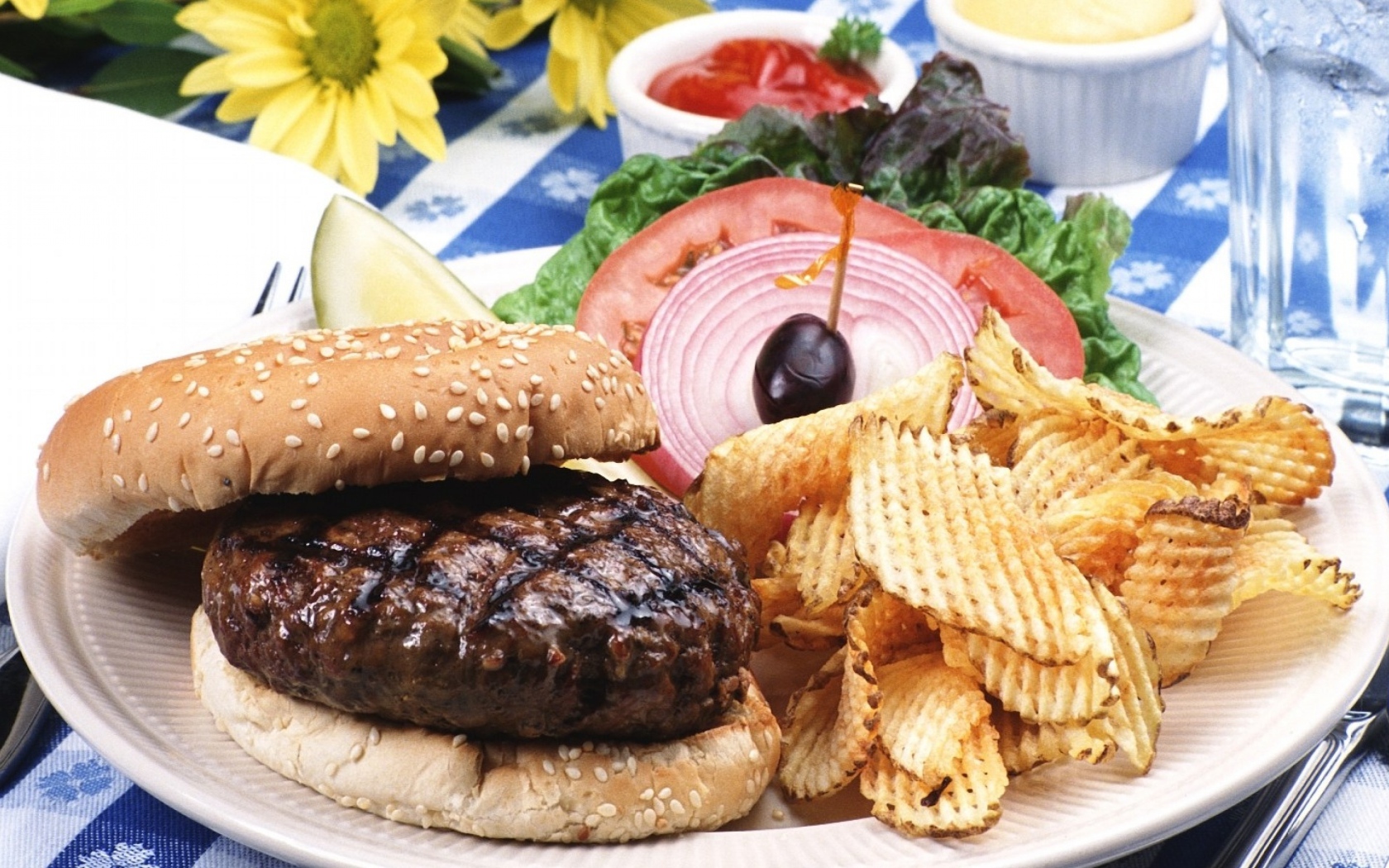 Гамбургер с котлетой и картофельные чипсы на тарелке с овощами