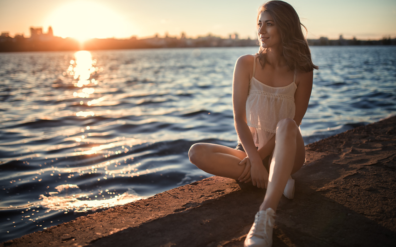 Красивая улыбающаяся девушка сидит в лучах солнца у реки