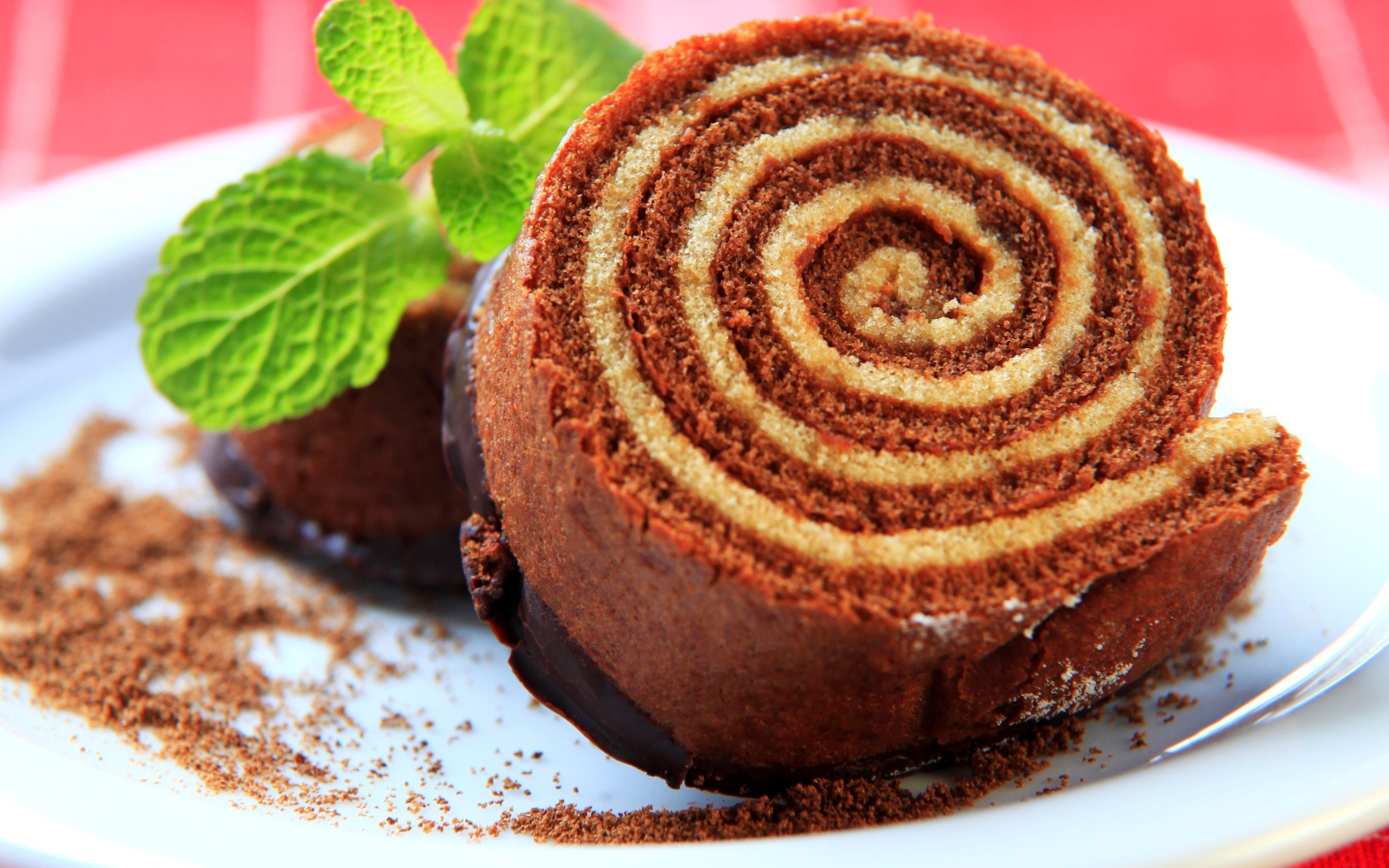 Кусок сладкого рулета с шоколадом и листом мяты на тарелке