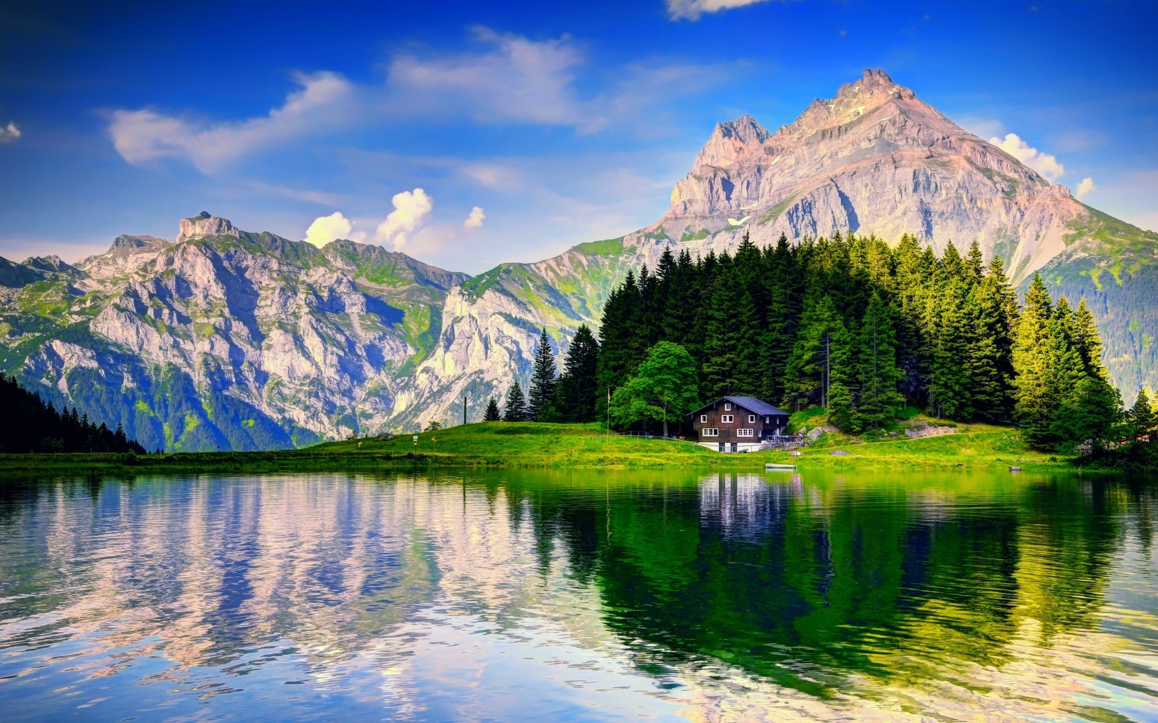 Лес и горы отражаются в озере под красивым голубым небом с белыми облаками