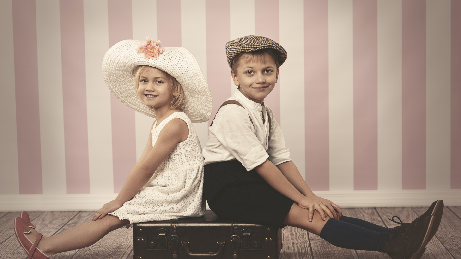 A girl in a big white hat and a boy are sitting on a suitcase
