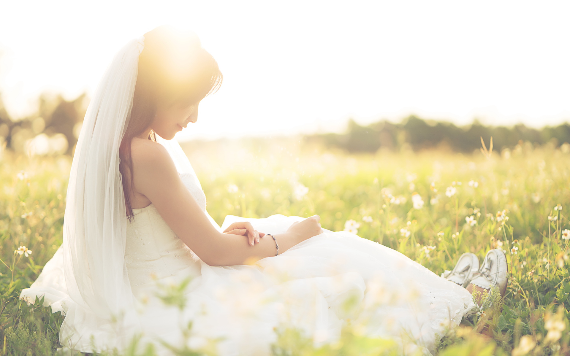 Девушка азиатка в платье невесты сидит на траве в поле 
