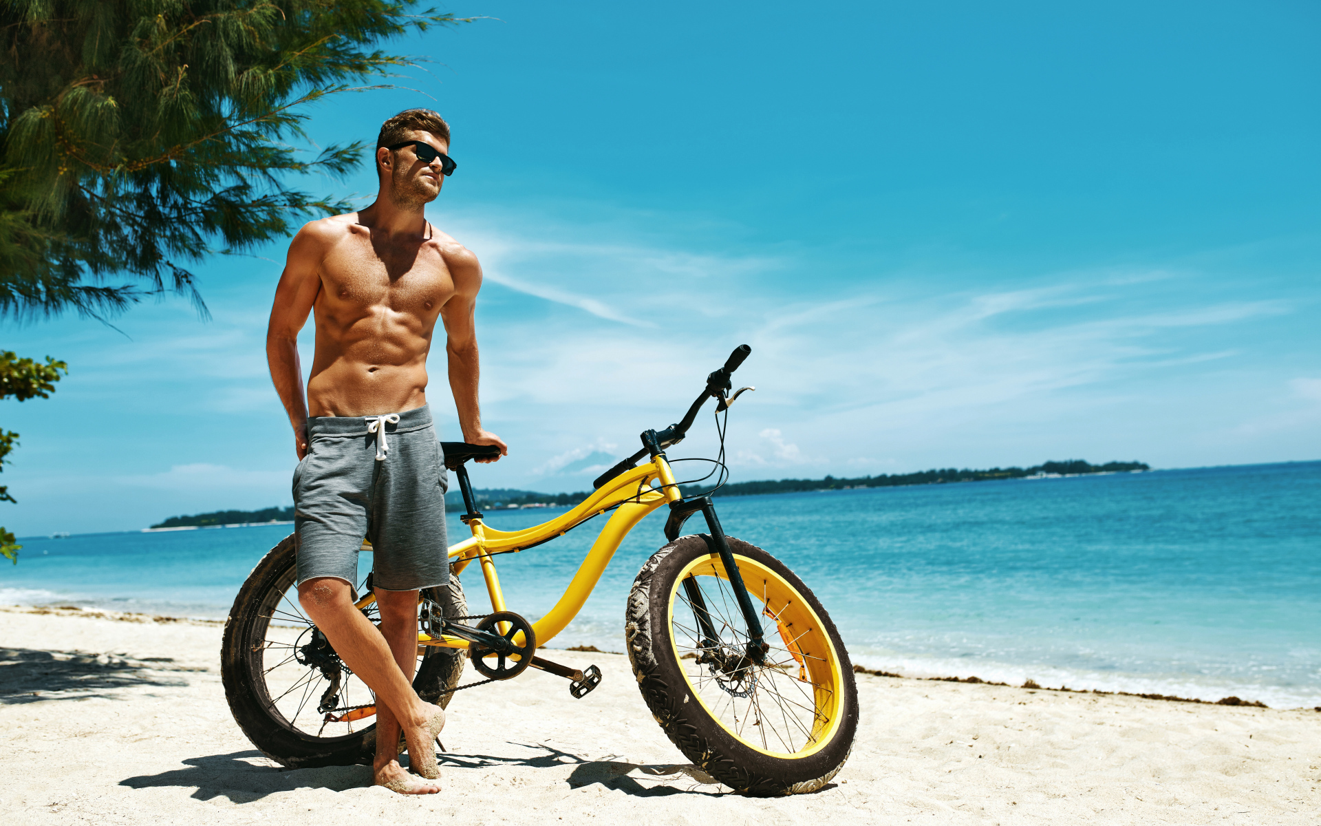 Красивый мускулистый парень с велосипедом на пляже