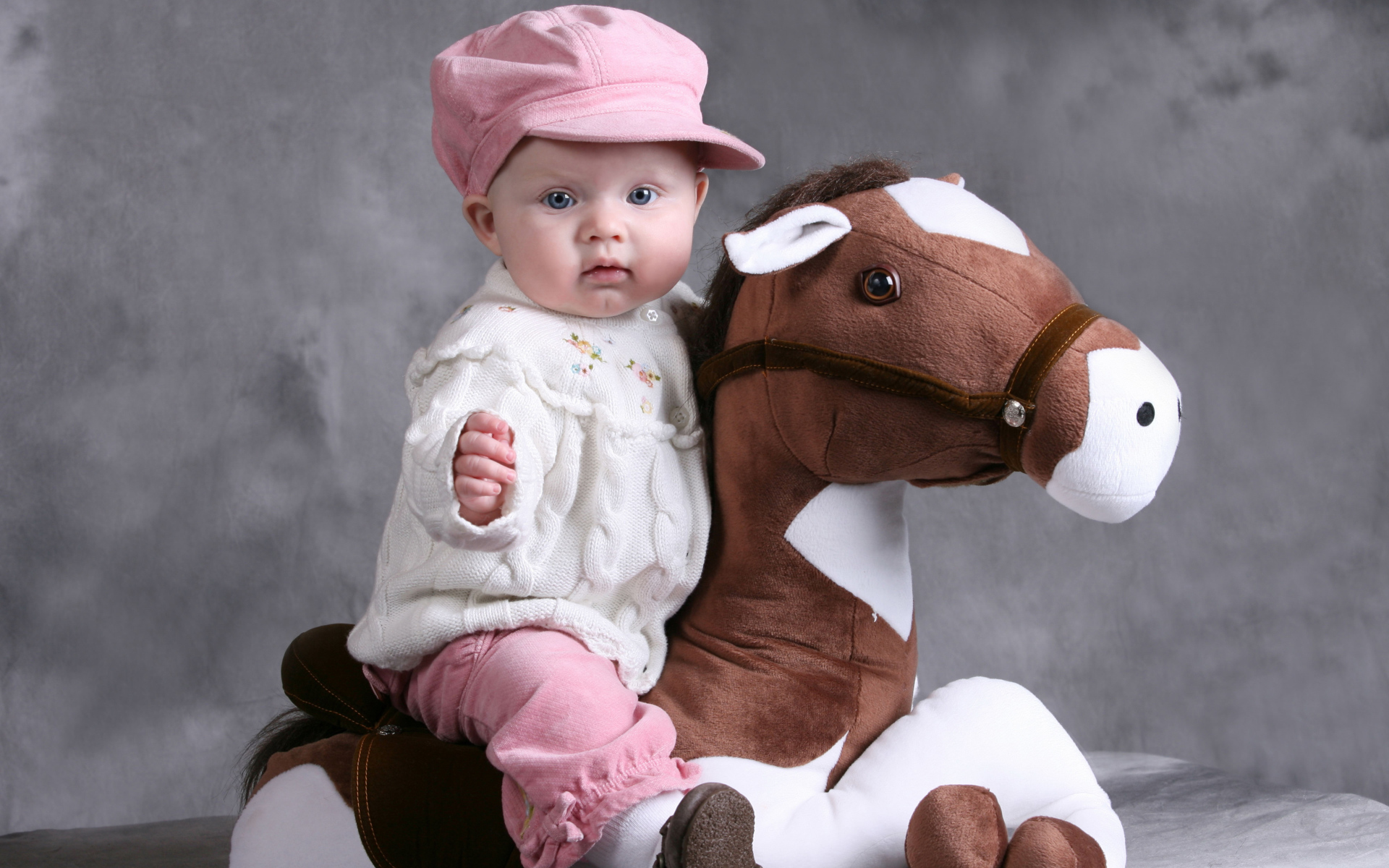 Маленький ребенок в розовой кепке сидит на игрушечной лошади