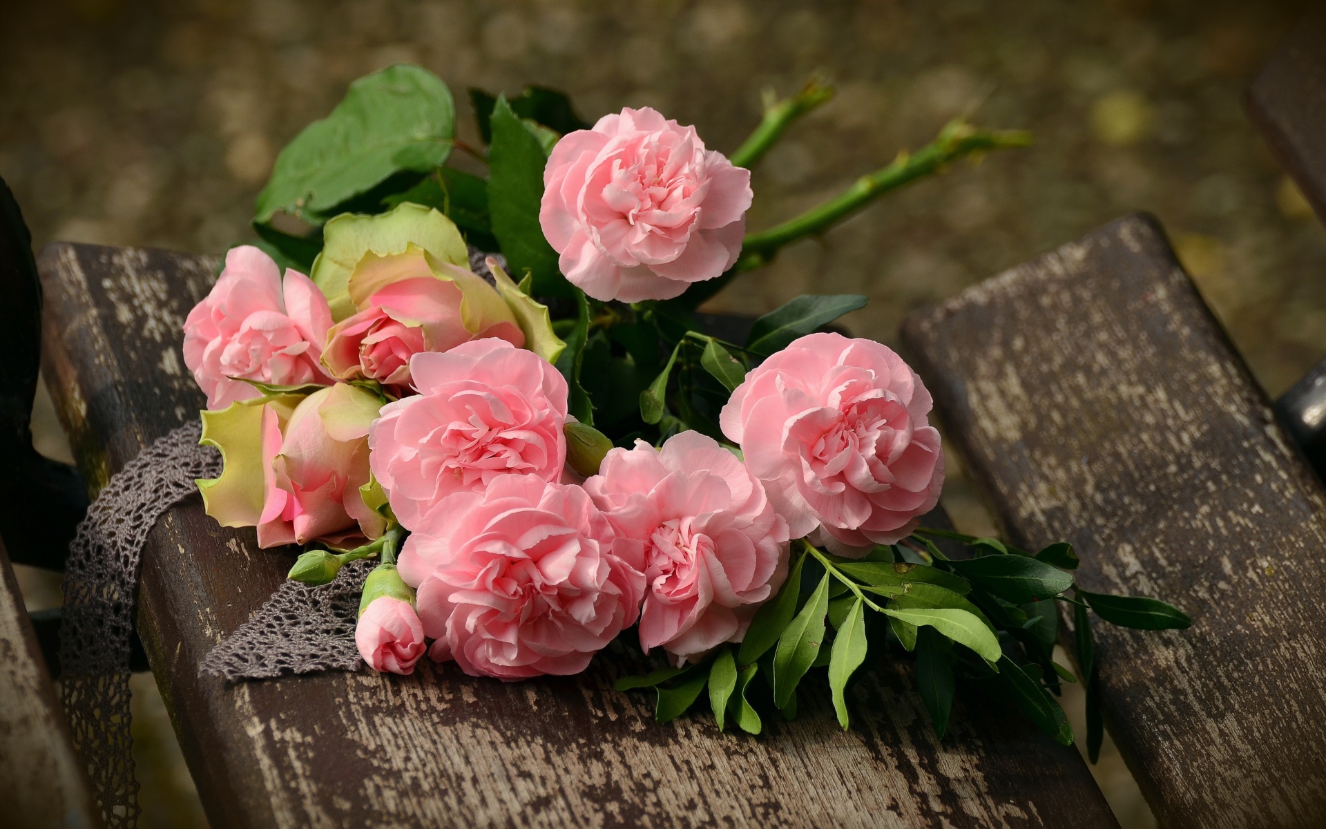 A bouquet of beautiful delicate pink roses lies on a wooden bench