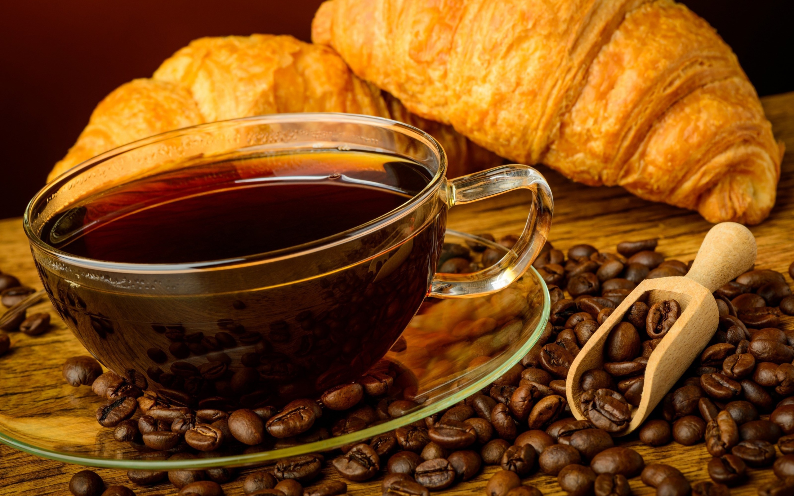 Glass cup of coffee with grains and fresh croissants on the table