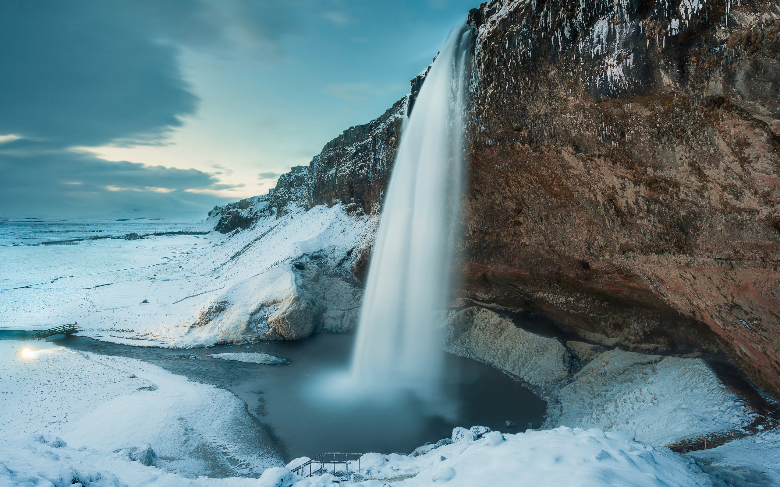 The waterfall drains from a cliff against a background of snow-covered nature, Iceland