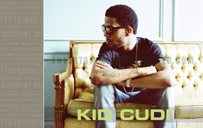 Kid Cudi is sitting on the yellow couch