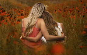 Two girls sit embracing in a field