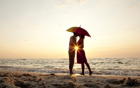 A loving couple on the beach is standing under an umbrella at sunset