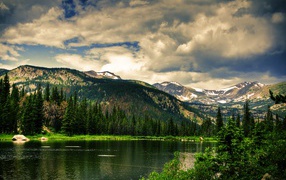 Чистое горное озеро на фоне покрытых лесом гор под облачным небом
