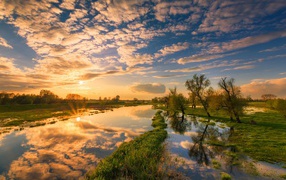 Восход солнца и облака отражаются в чистой воде реки 