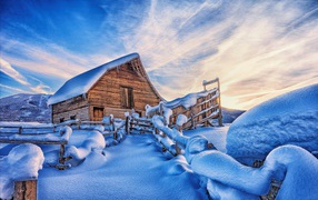 A snow-covered house in the mountains under a beautiful sky