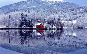 House, forest and mountain reflect in the lake in winter