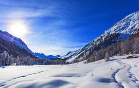 The winter sun in the blue sky over the snow-capped mountains