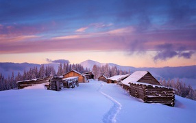 Wooden houses are covered with snow on the background of mountains in winter