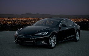 Черный стильный электромобиль Tesla Model S на фоне ночного мегаполиса 