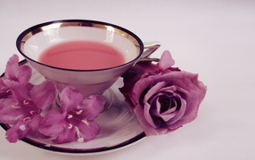 Чашка чаю на тарелке с розой и колокольчиками на сером фоне