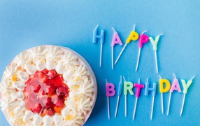 Beautiful cake with cream and strawberries on a blue background with candles for birthday