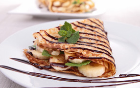Thin sweet pancakes with bananas and chocolate on a white big plate treat to Shrovetide