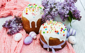 Easter cakes with sugar icing on the table with dyed eggs and a bouquet of lilac on Easter