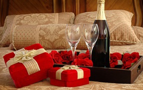 A bottle of wine, two glasses and gifts for a romantic evening on the bed