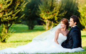 Happy bride and groom are sitting on green grass