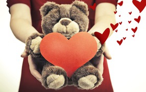 Плюшевый медведь с большим красным сердцем в руках