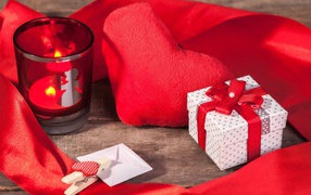 Мягкое красное сердце на столе с подарком и зажженной свечей