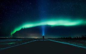 A man walks on the road at night against the background of the northern lights