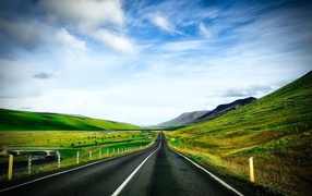 Ровная дорога у зеленых холмов на фоне голубого неба