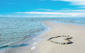 Heart of stones on the sand by the calm sea under the blue sky