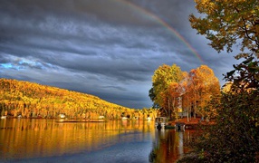 Rainbow in the cloudy sky above the lake near the autumn forest