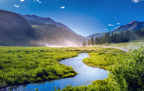 Речка на фоне покрытых зеленью гор под голубым небом