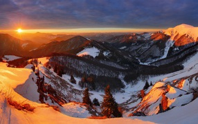 Snow-covered mountains covered with trees in the sun at sunset
