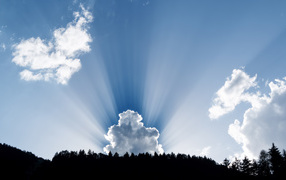 The sun's rays make their way through the white clouds in the blue sky