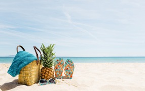 Bag, pineapple, slippers and sunglasses are lying on the sand on the beach in summer
